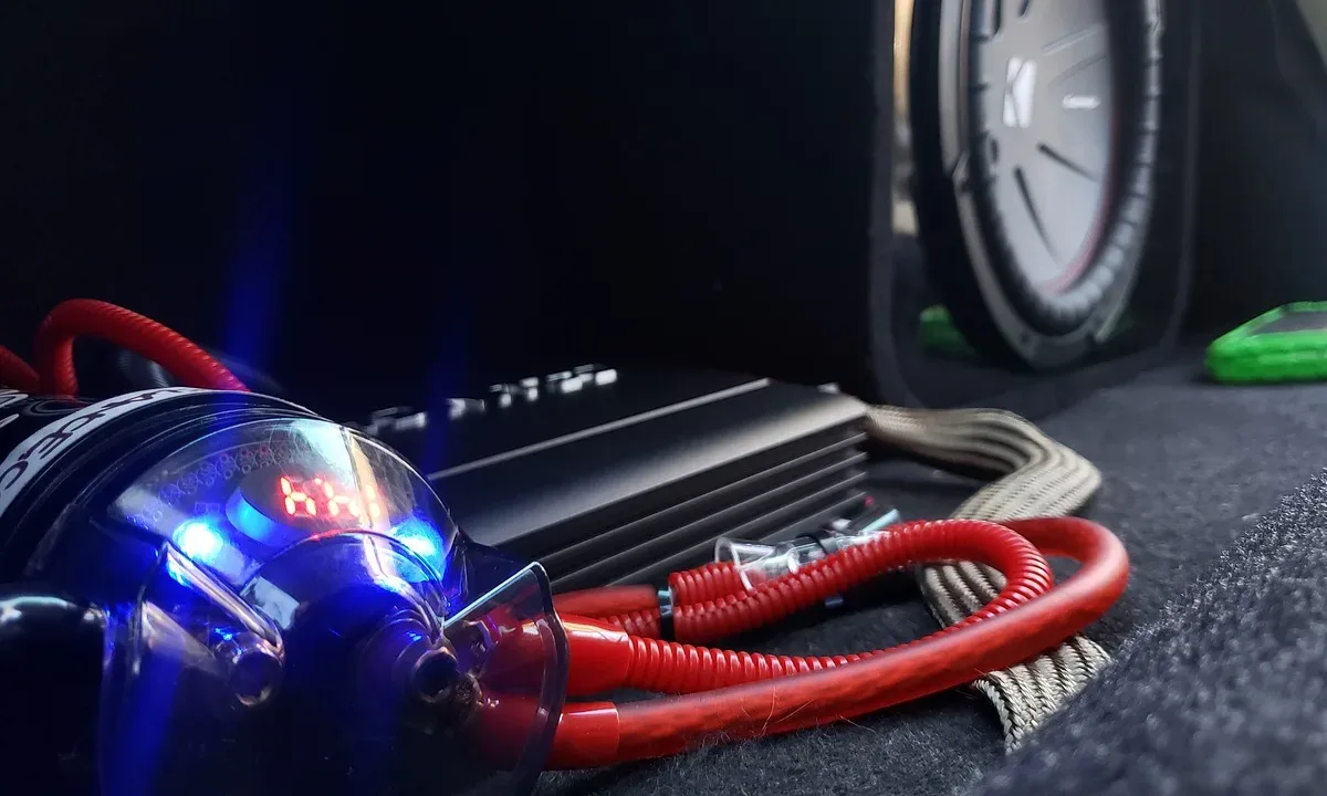 How to choose an amplifier for car speakers: a car amplifier with red power cables and a capacitor installed in a trunk