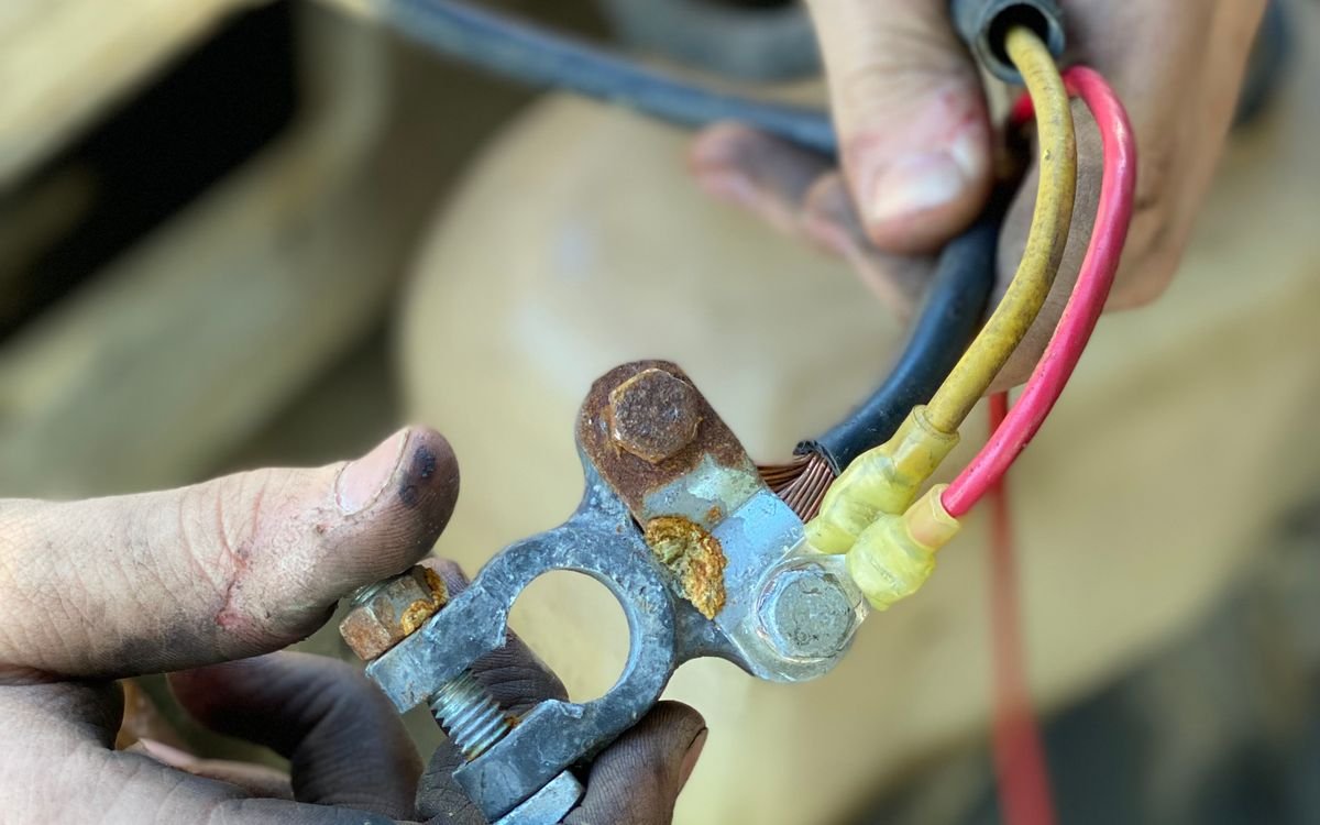 Hands working on a corroded battery terminal with several wires attached