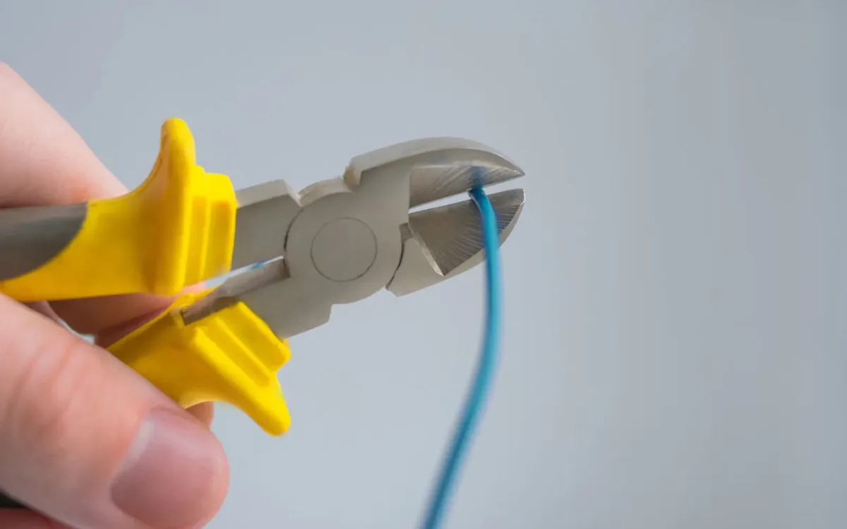 Pliers cutting a blue wire, showing how to install crossover car audio wiring