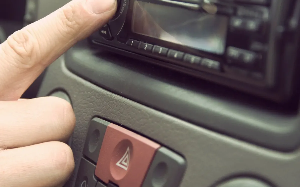 Finger pressing a car stereo button to show how to use a crossover car audio setup