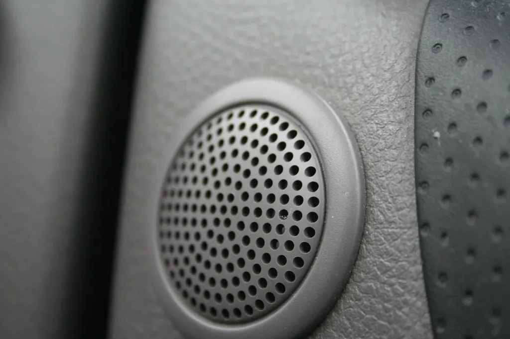 Round plastic speaker grille with small perforations in a car interior panel