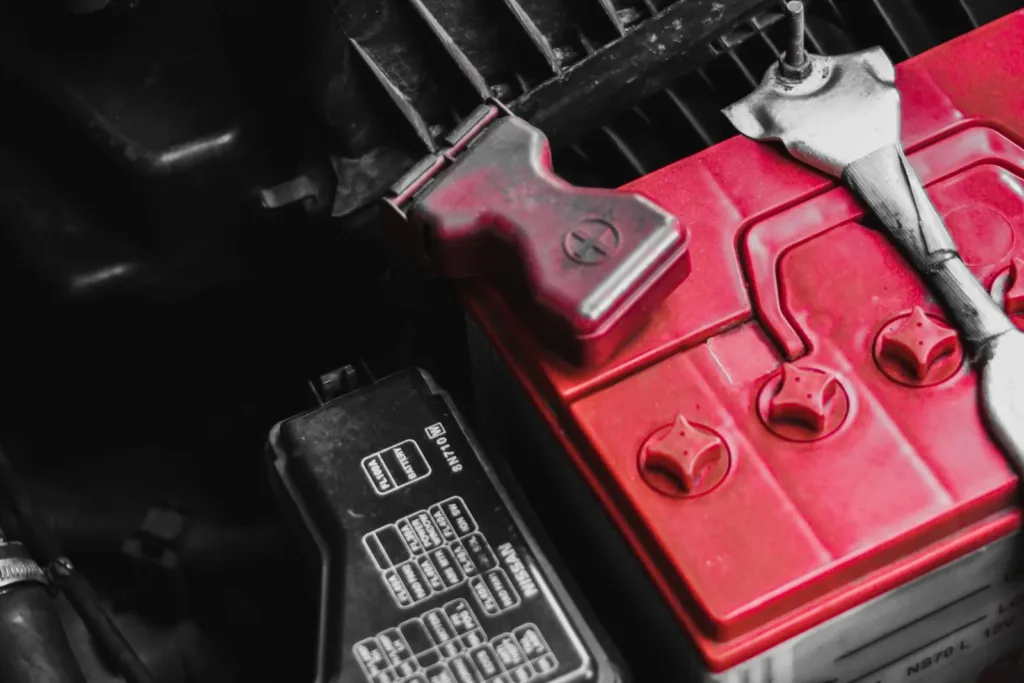Car battery with a red positive terminal cover in an engine bay